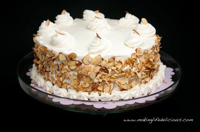 a cake with white frosting and almonds on top sitting on a glass plate