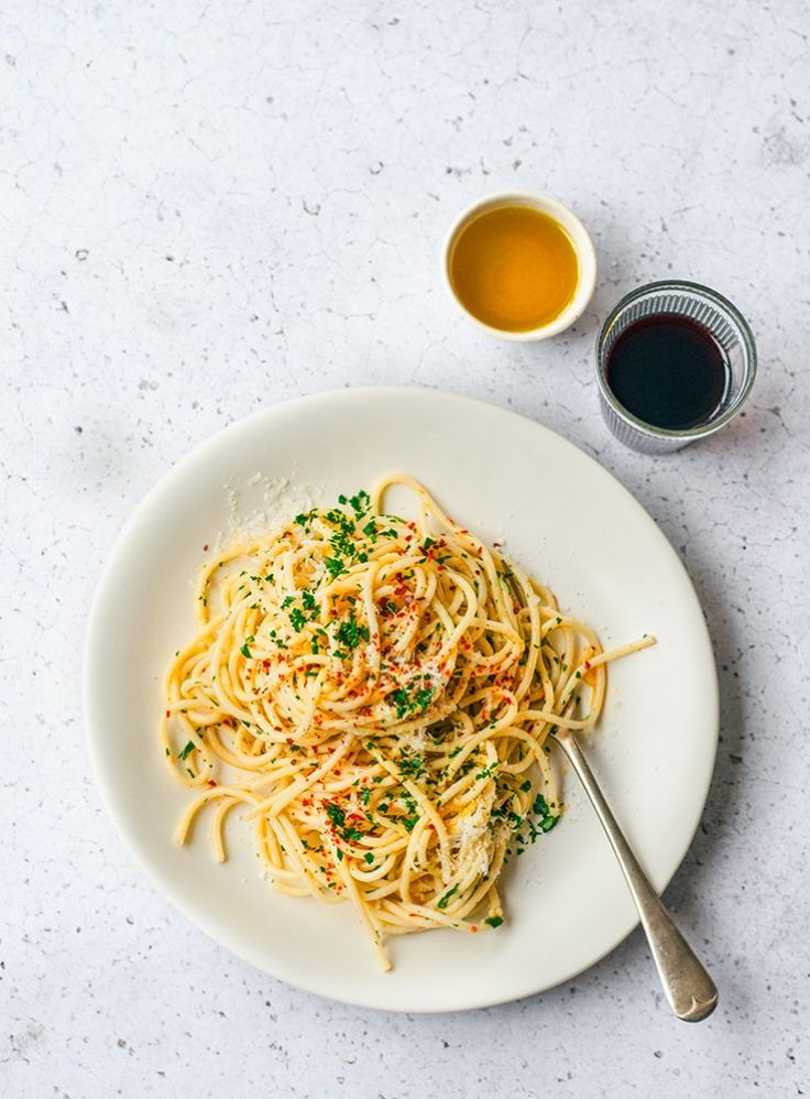 a white plate topped with pasta and sauce next to a cup of tea on top of a table