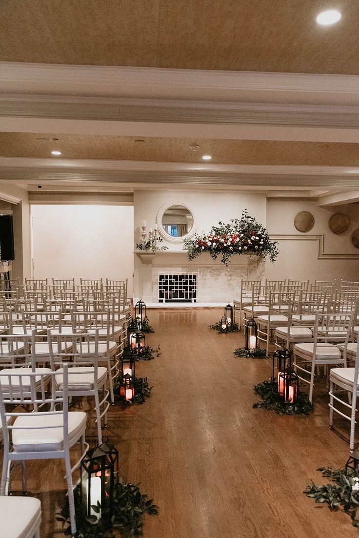 an empty room with white chairs and candles on the floor in front of it is decorated with greenery