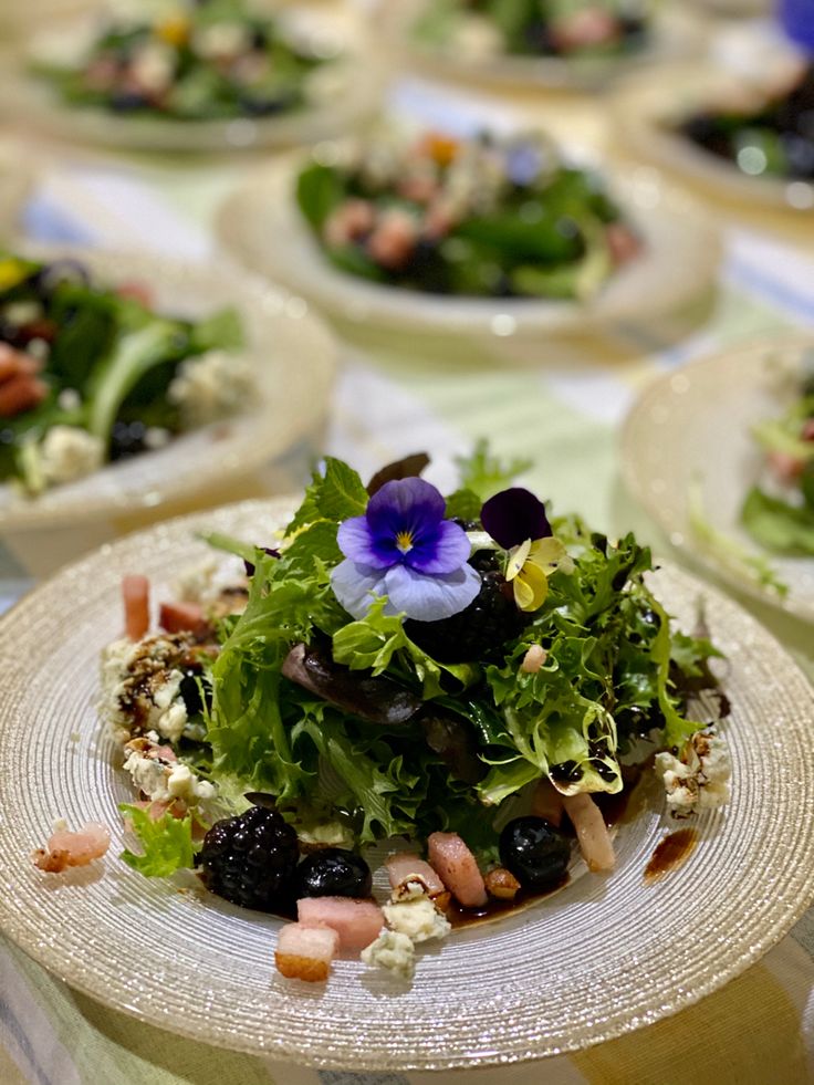 several plates filled with different types of salads on top of a tablecloth covered table