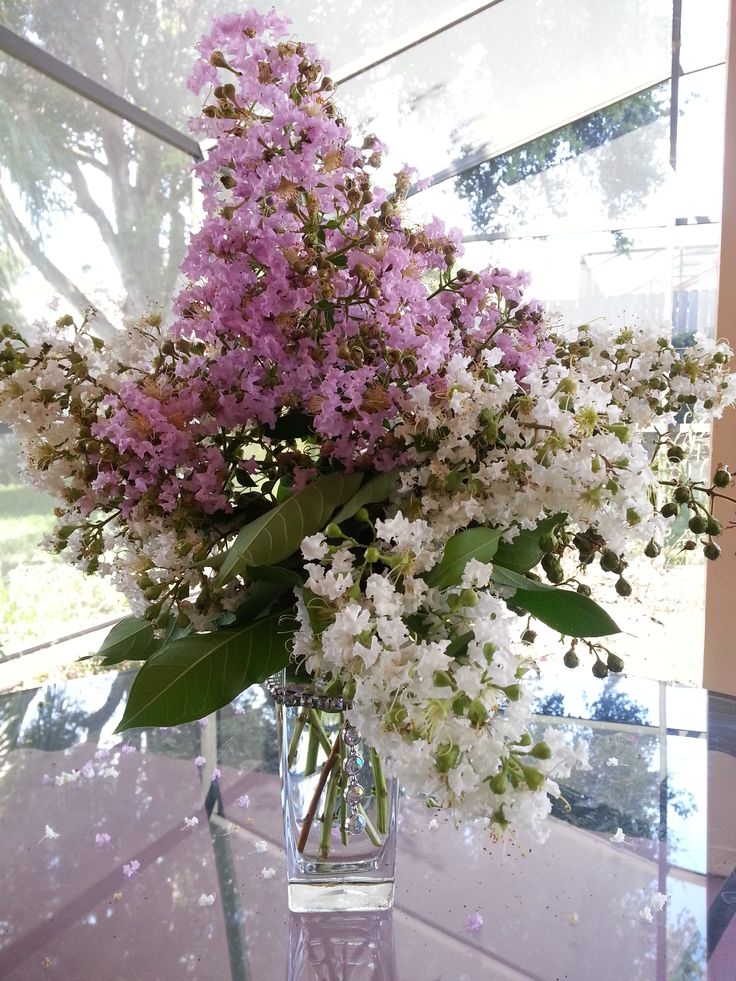 a vase filled with lots of purple and white flowers on top of a glass table