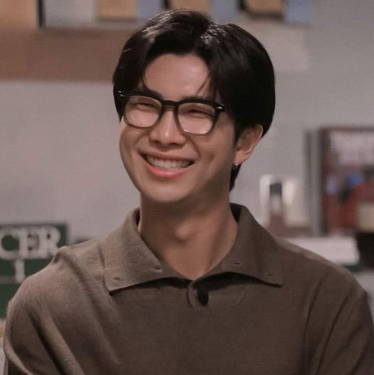 a young man wearing glasses and smiling at the camera while standing in front of a counter