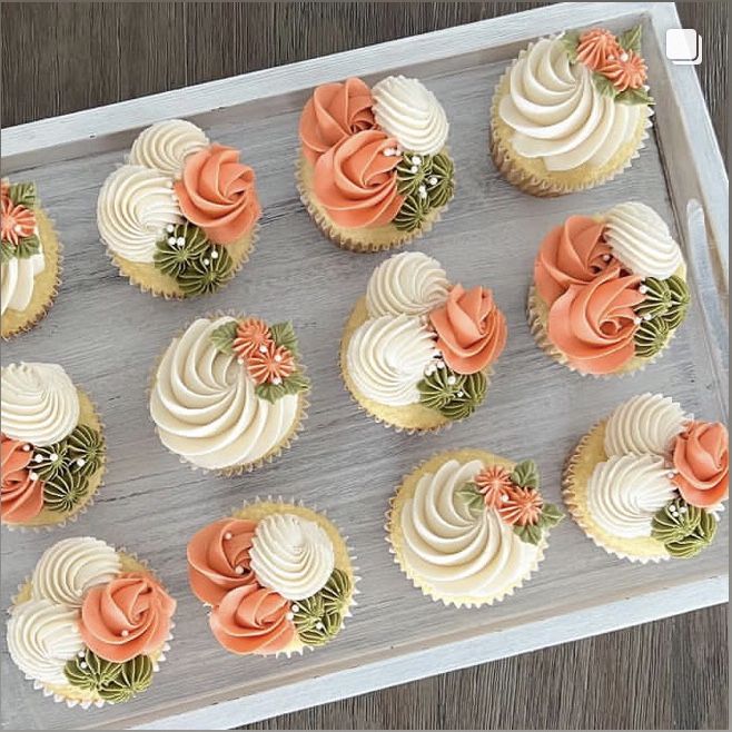 cupcakes with white frosting and orange flowers are arranged in rows on a tray