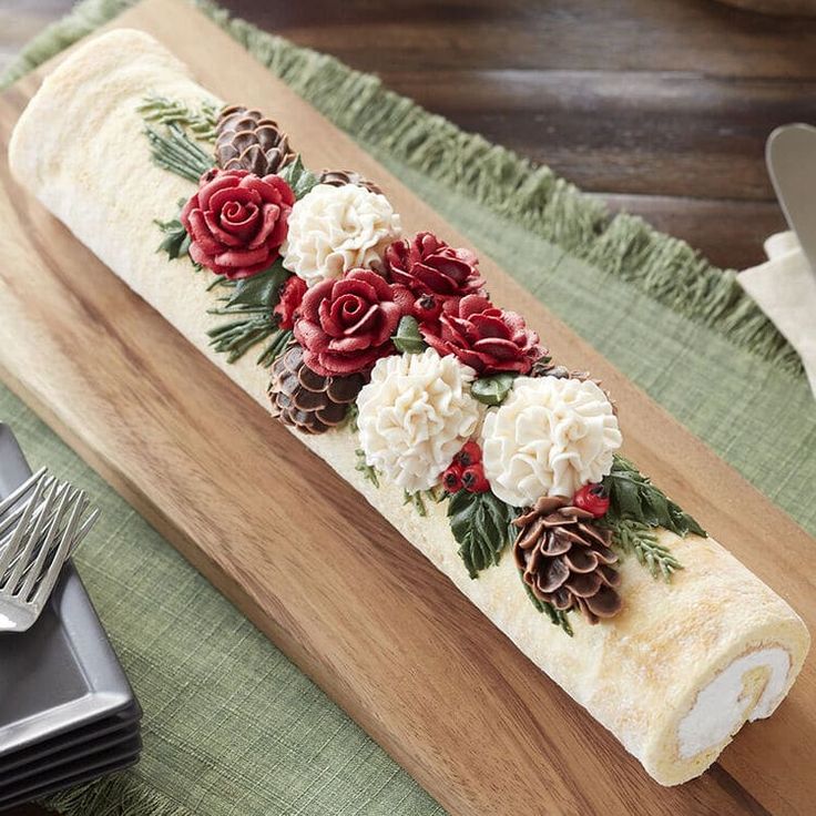 a roll decorated with flowers and pine cones on top of a wooden board next to silverware