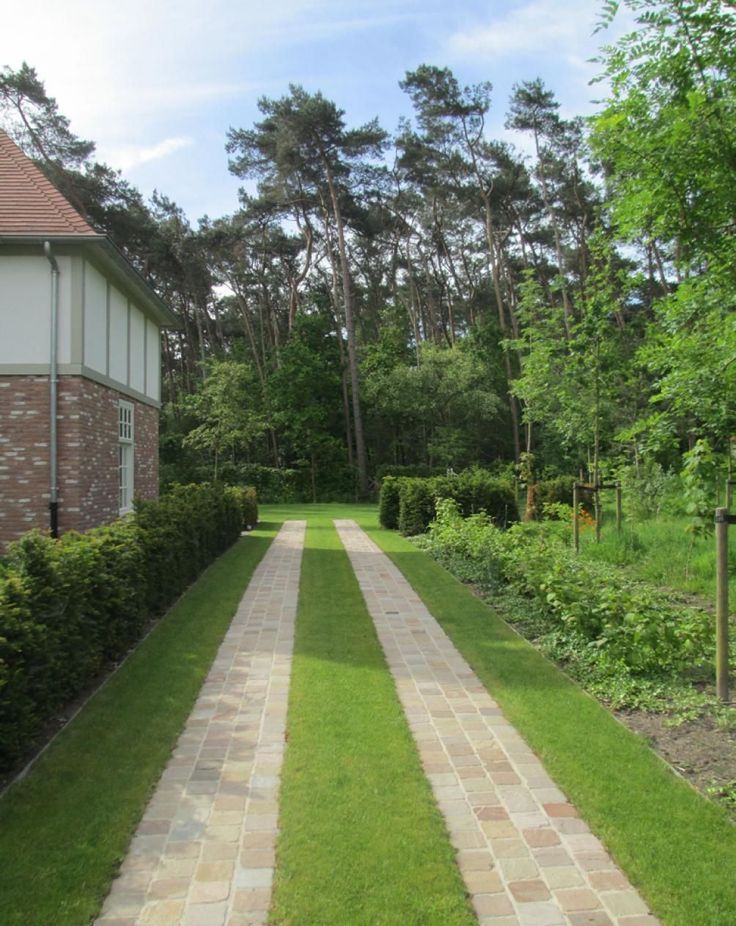 a brick walkway in the middle of a lush green yard with trees and bushes on either side