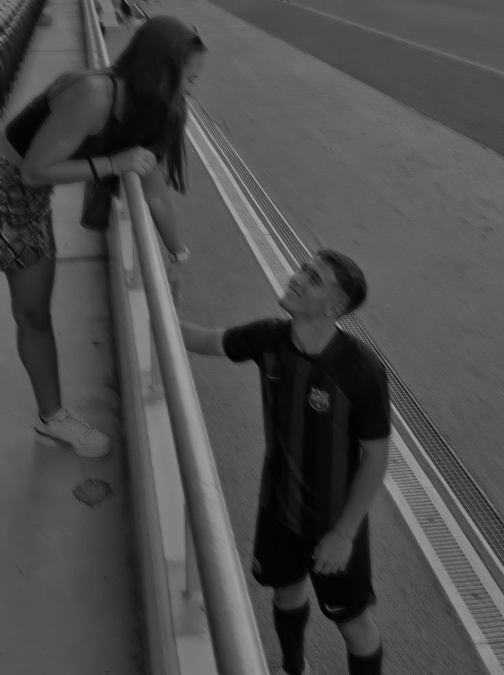 a young boy standing next to a woman on the side of a road while holding onto a skateboard