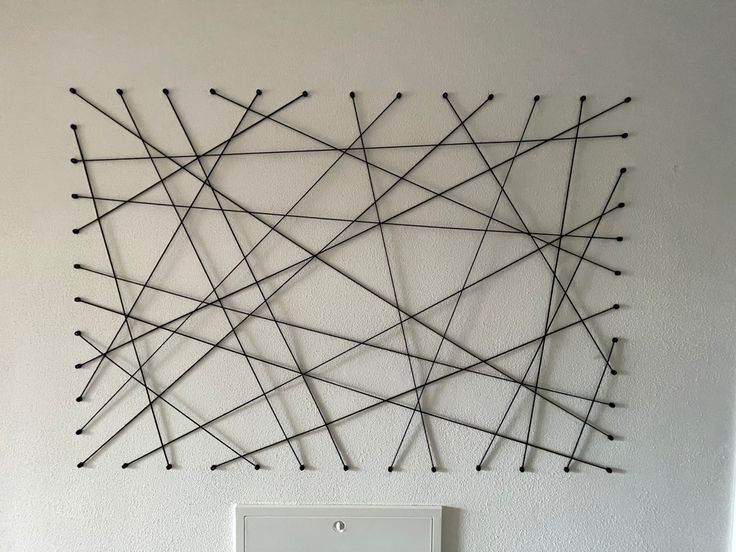 a wall sculpture made out of sticks on the side of a white wall next to a light switch