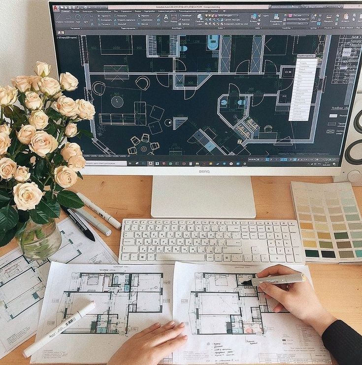 a person is working on architectural drawings in front of a computer screen with roses and other office supplies