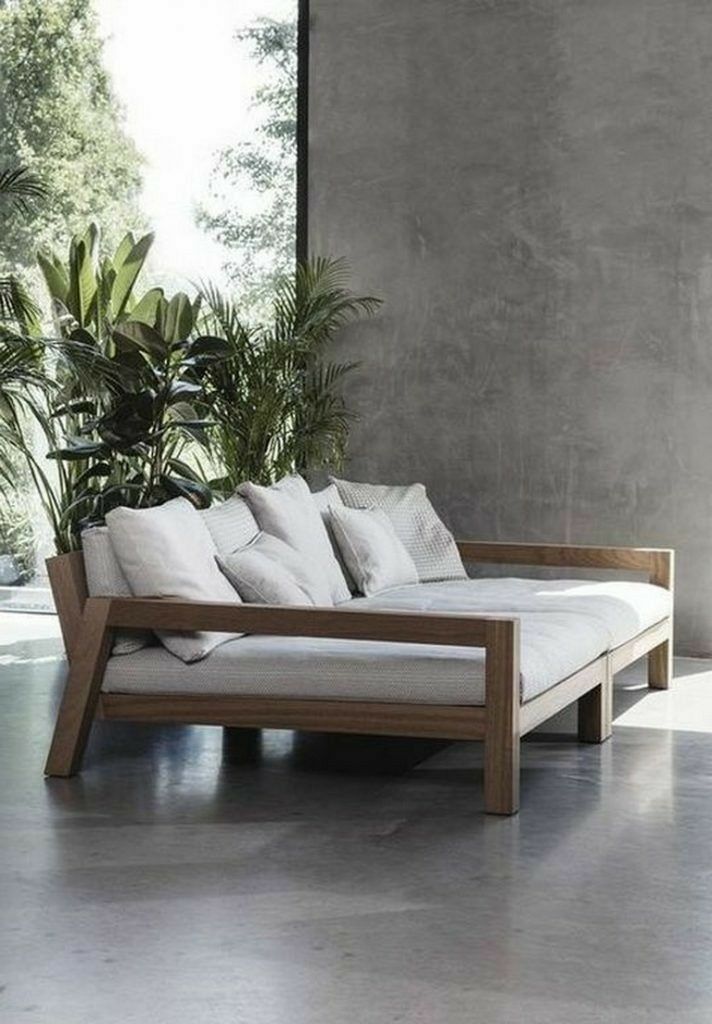 a white couch sitting next to a plant on top of a cement floor in front of a wall