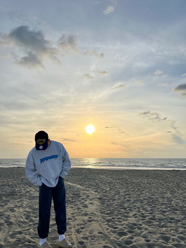 a man standing on top of a sandy beach next to the ocean under a cloudy sky