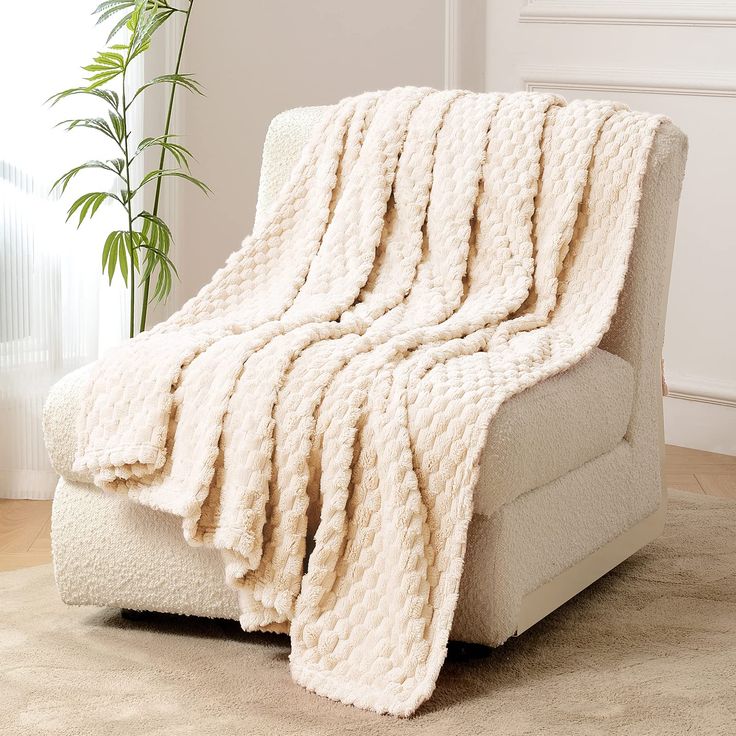 a white couch with a blanket on it in a room next to a potted plant