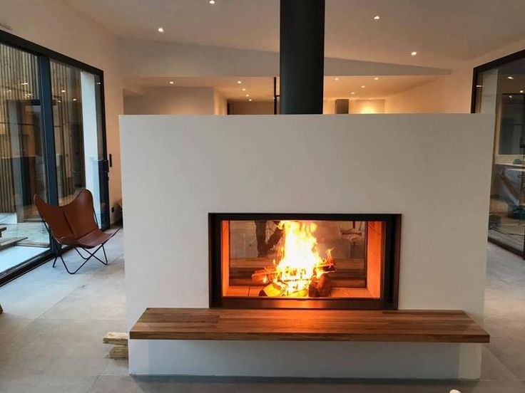 a fire place in the middle of a living room with glass doors and large windows