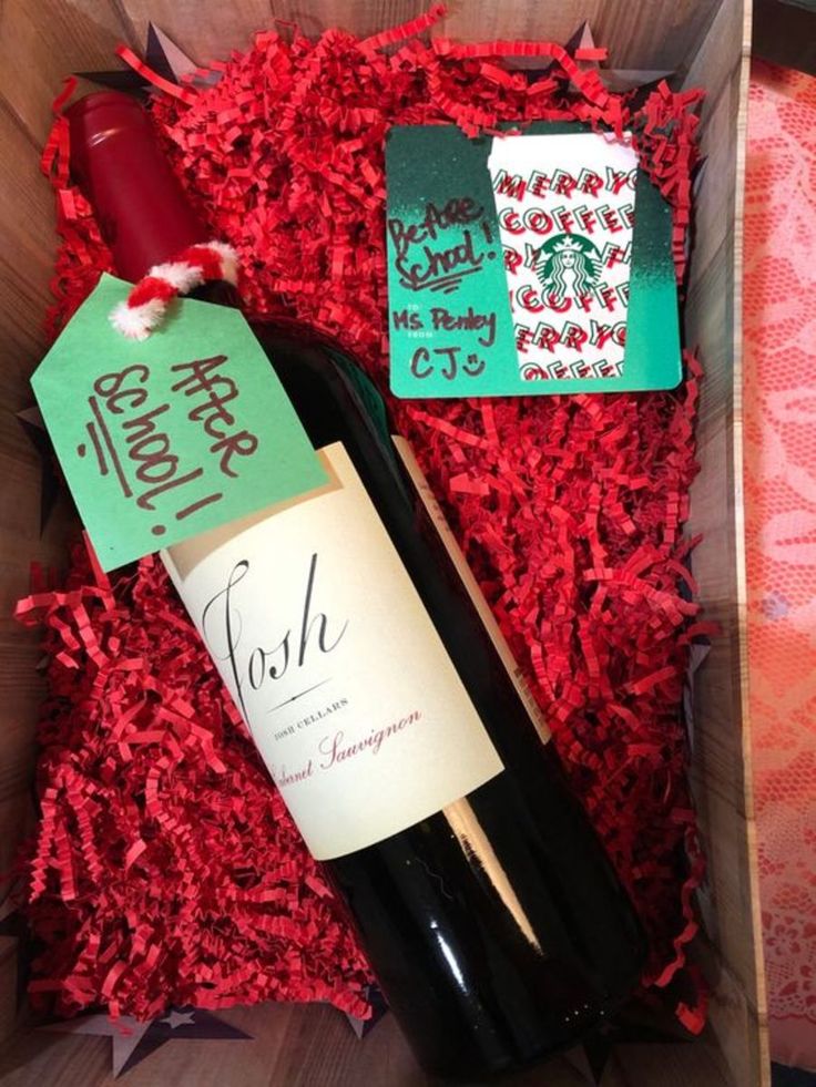 a bottle of wine in a wooden box with red shredded paper and tags on it