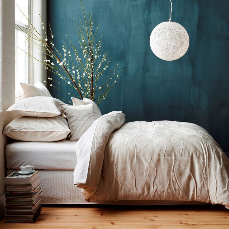 a bedroom with teal walls and white linens on the bed, along with a plant