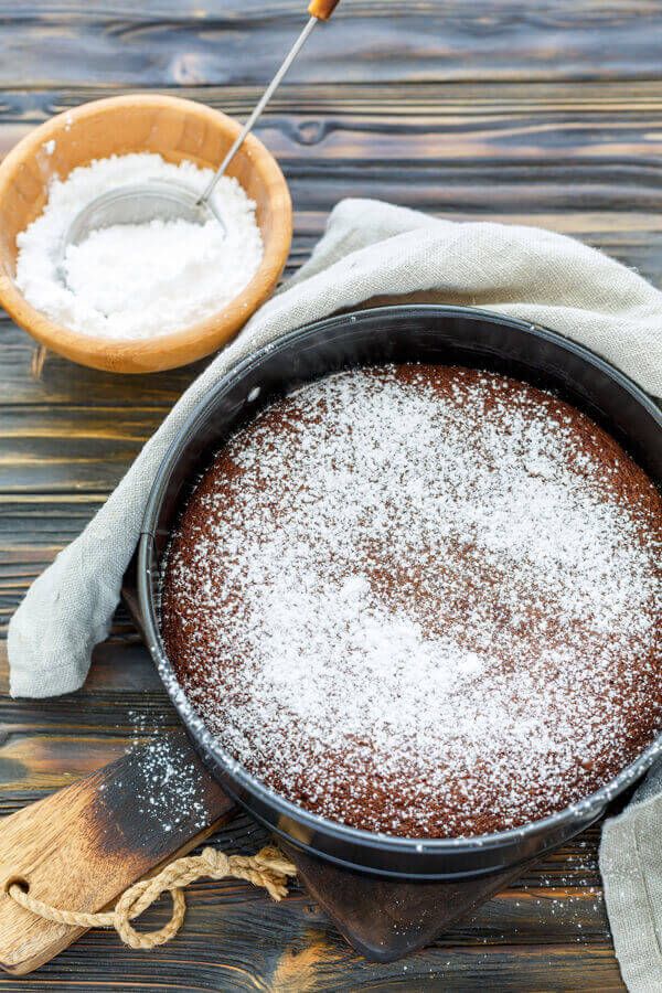 a cake in a pan with powdered sugar on top and a wooden spoon next to it