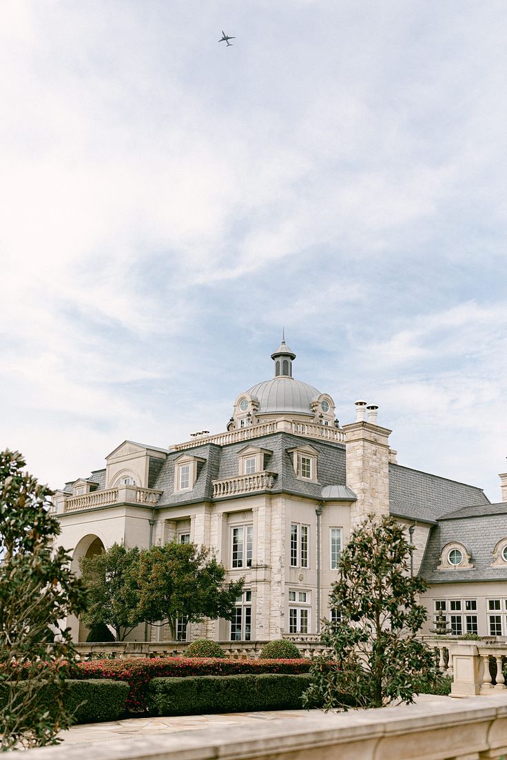 a large white building with a plane flying in the sky over it's roof