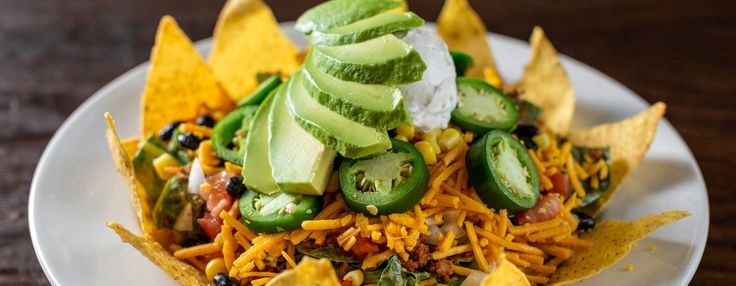 a white plate topped with nachos covered in cheese and toppings on top of tortilla chips