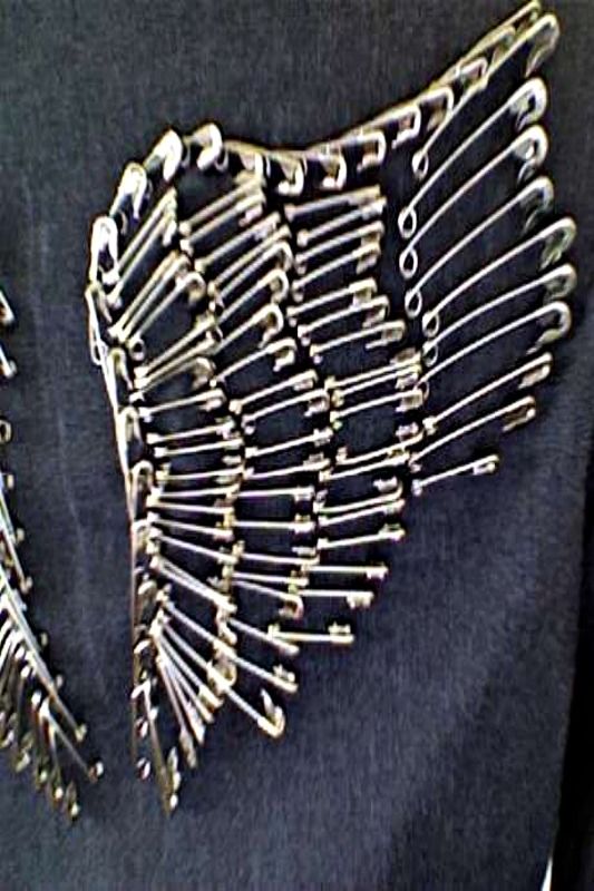 the back of a woman's shirt with metal pins attached to her chest and an intricate design on it