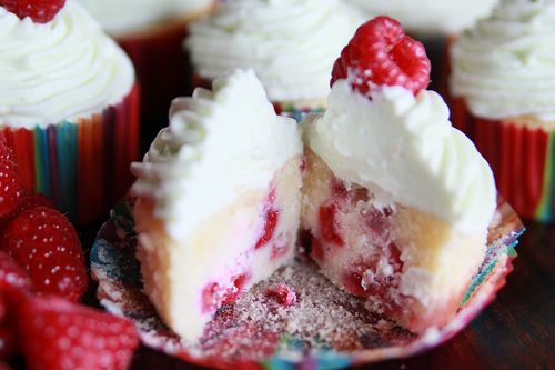 some cupcakes with white frosting and raspberries on top