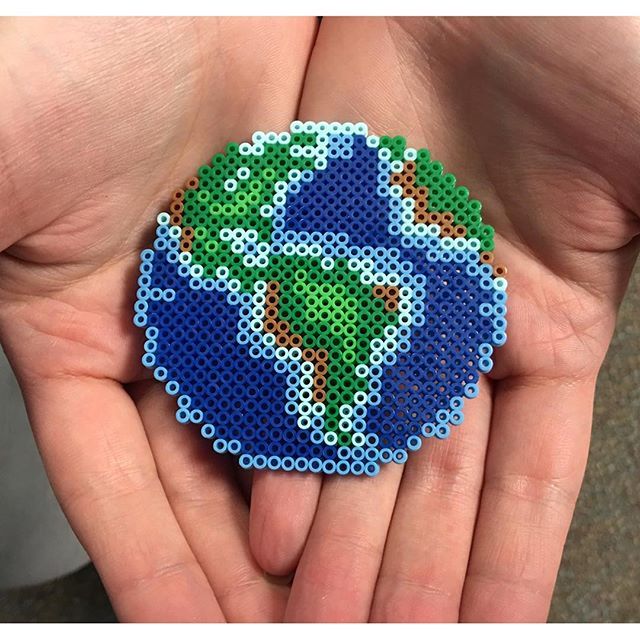 a hand holding a small beaded brooch in the shape of a planet on it's palm