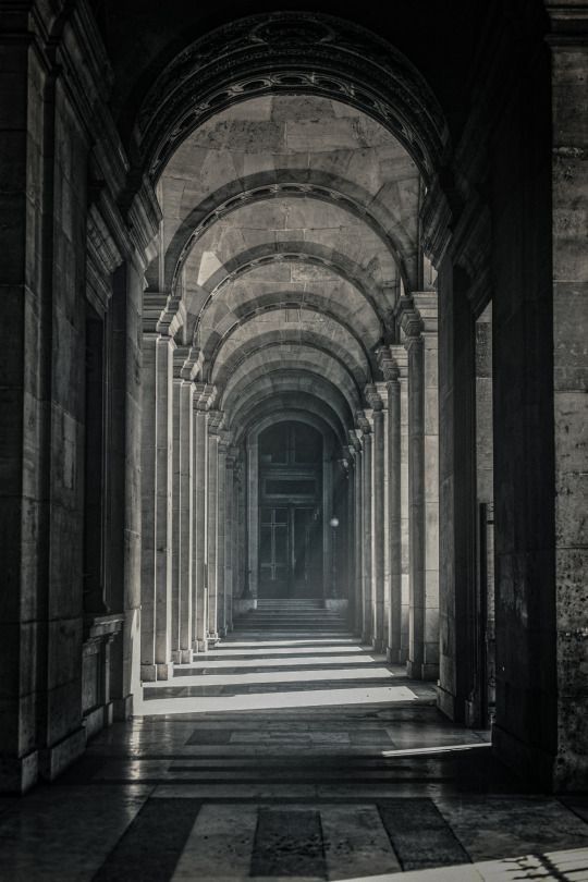 black and white photograph of an arched hallway with stone columns, light coming through the doorways