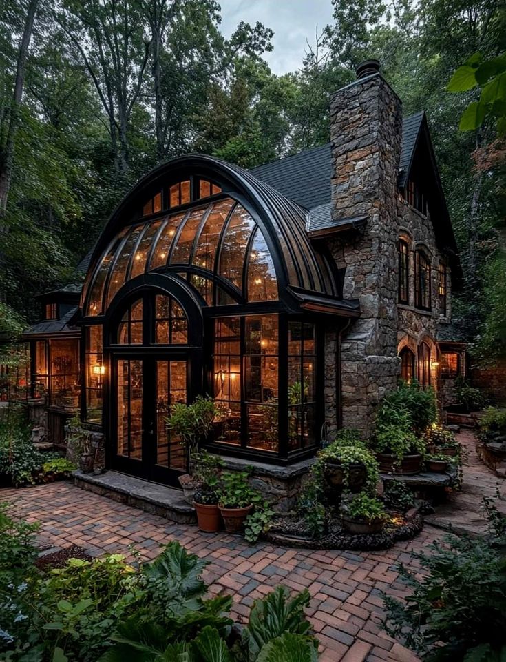 a large glass house in the middle of a forest with lots of trees and plants around it