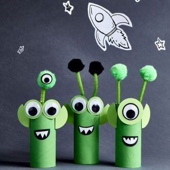 three green toys with eyes and mouths are lined up in front of a space rocket