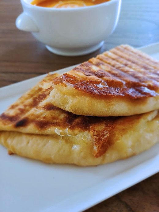 three pancakes on a white plate next to a bowl of orange sauce and a cup of soup