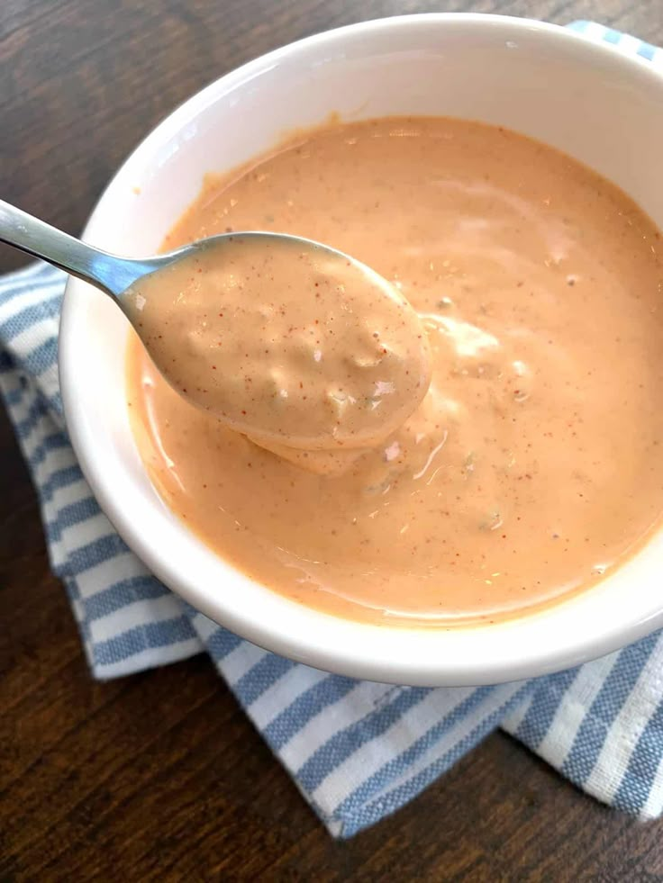 a spoon in a white bowl on top of a blue and white striped napkin with a brown sauce