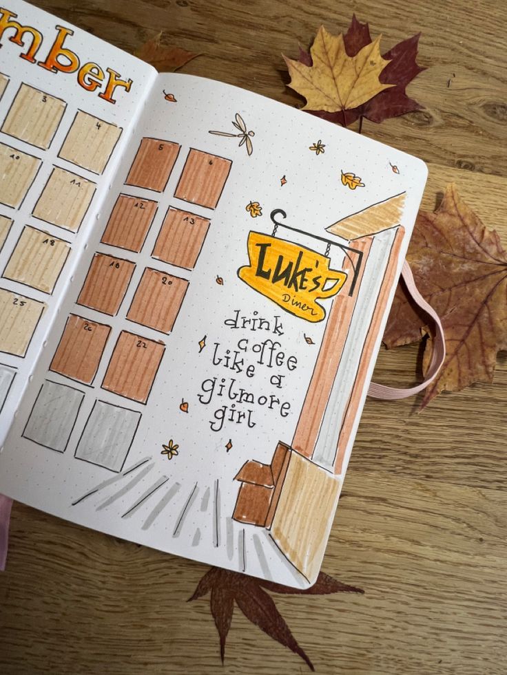 an open planner book sitting on top of a wooden table next to leaves and autumn leaves