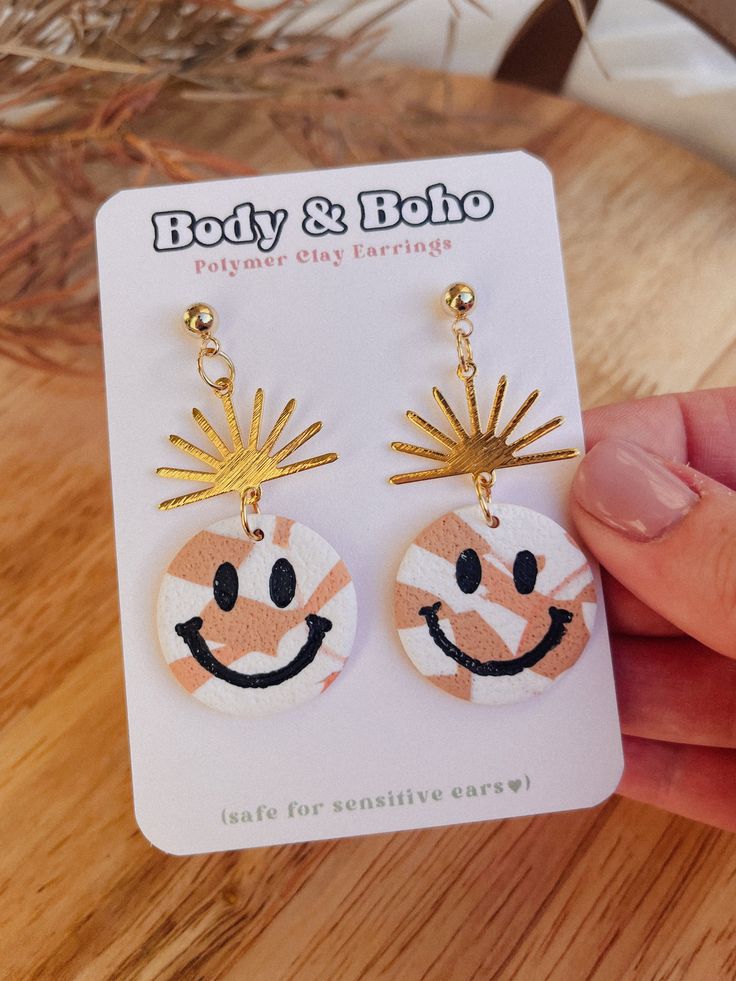 a pair of earrings with the face of a smiling person on it, in front of a wooden table