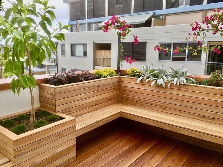 a wooden bench sitting on top of a wooden floor next to a planter filled with flowers