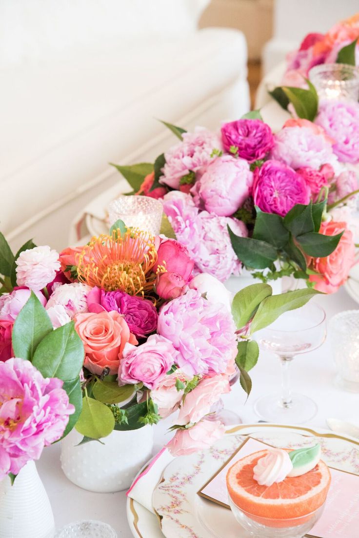 the table is set with pink and white flowers in vases, plates and silverware