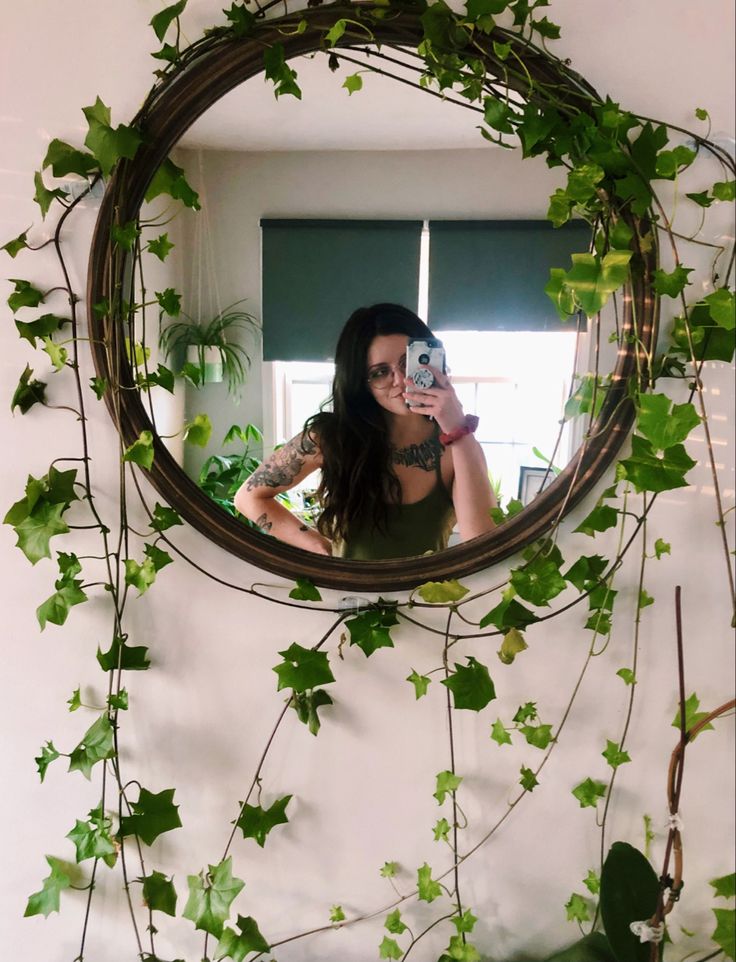 a woman taking a selfie in front of a mirror with ivy growing on it