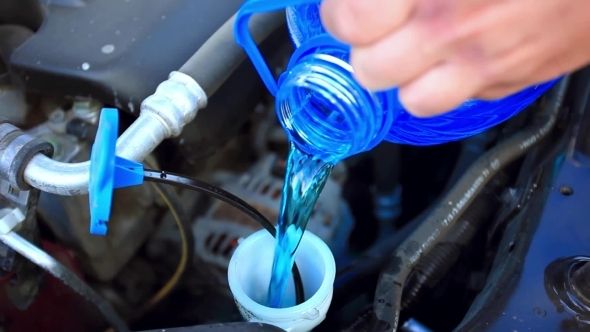 a person is pouring water from a hose into a car's engine