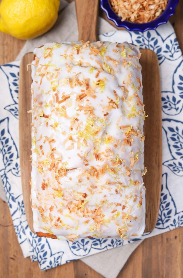 a loaf of lemon pound cake sitting on top of a wooden cutting board next to a bowl of granola