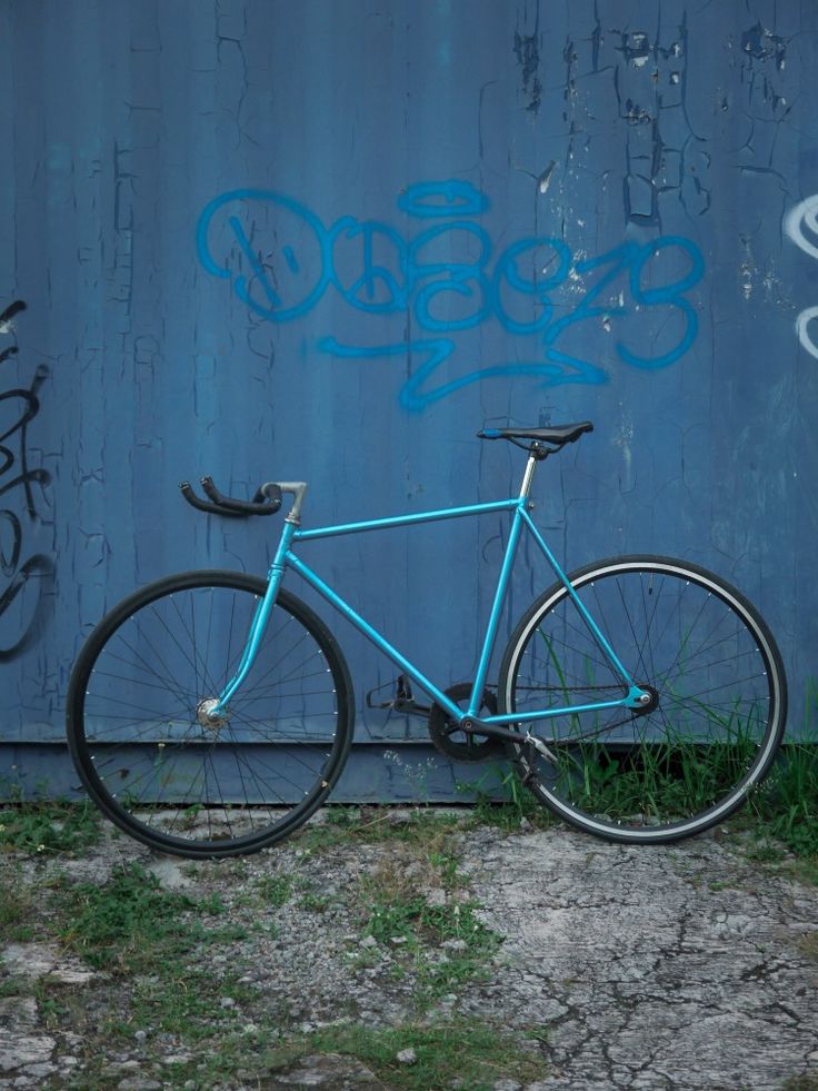 a blue bicycle parked in front of a wall with graffiti on it's side