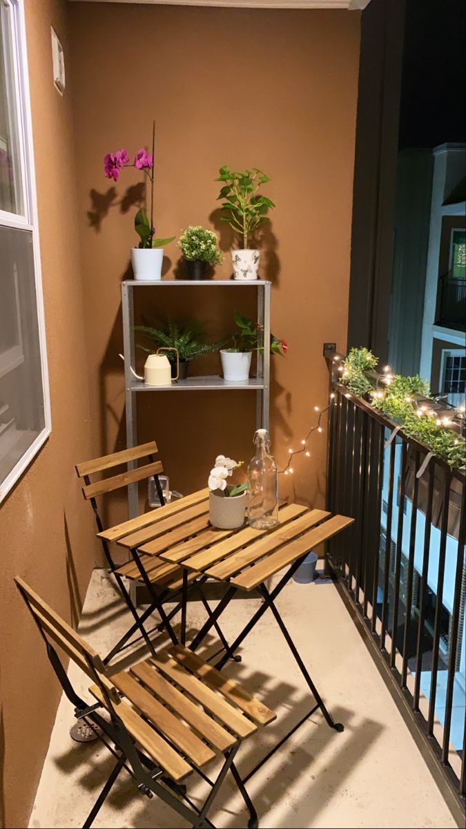 two wooden chairs sitting on top of a balcony next to a table and shelf filled with potted plants