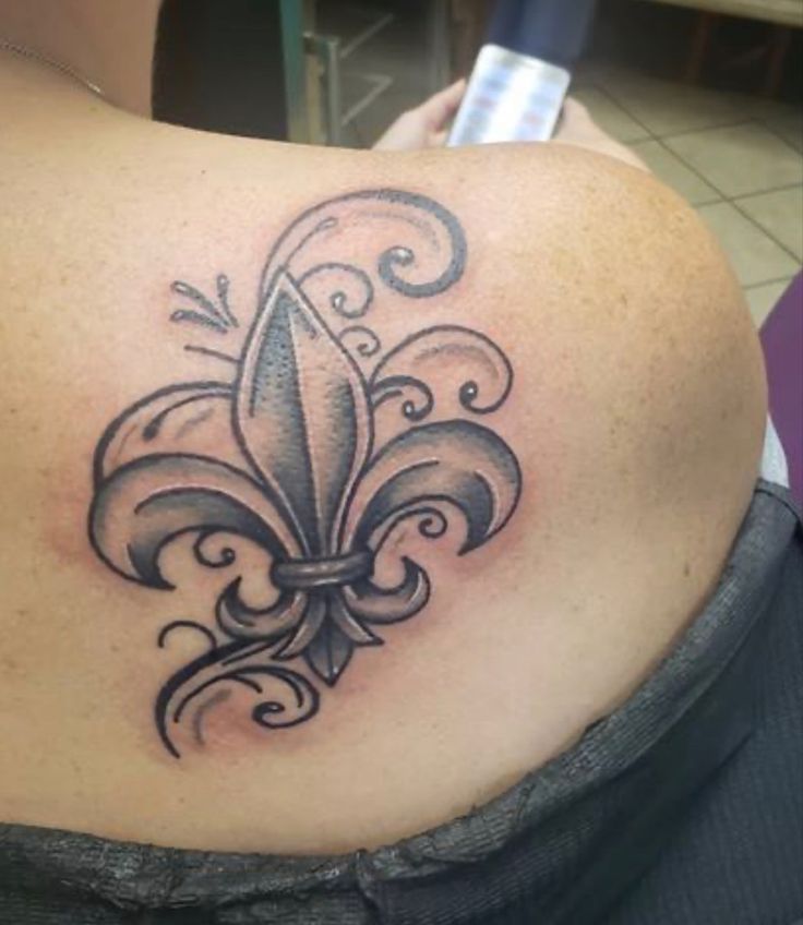 the back of a woman's shoulder with a fleur de lis tattoo on it