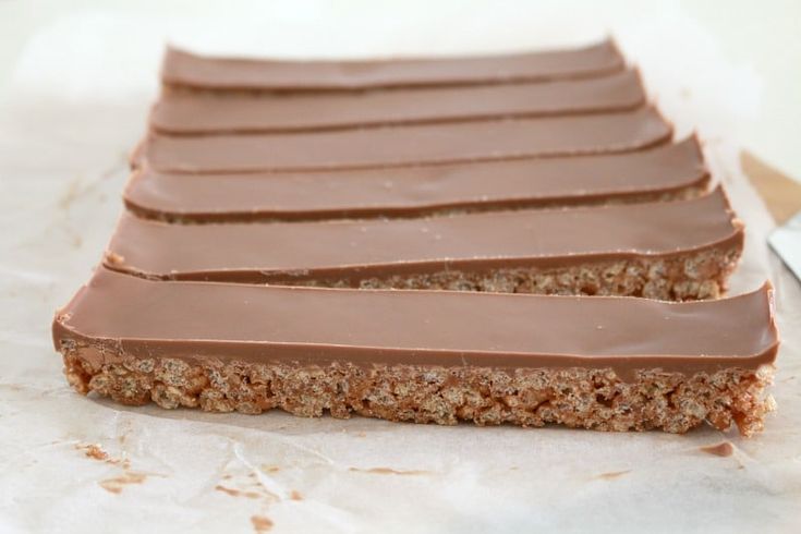 chocolate bars are lined up on top of parchment paper with a knife in the background