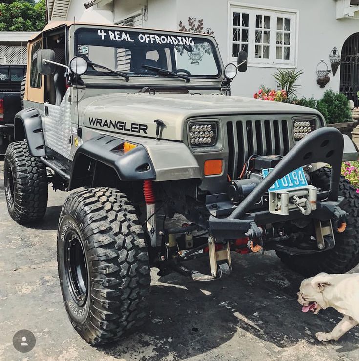 a dog laying on the ground next to a parked jeep in front of a house