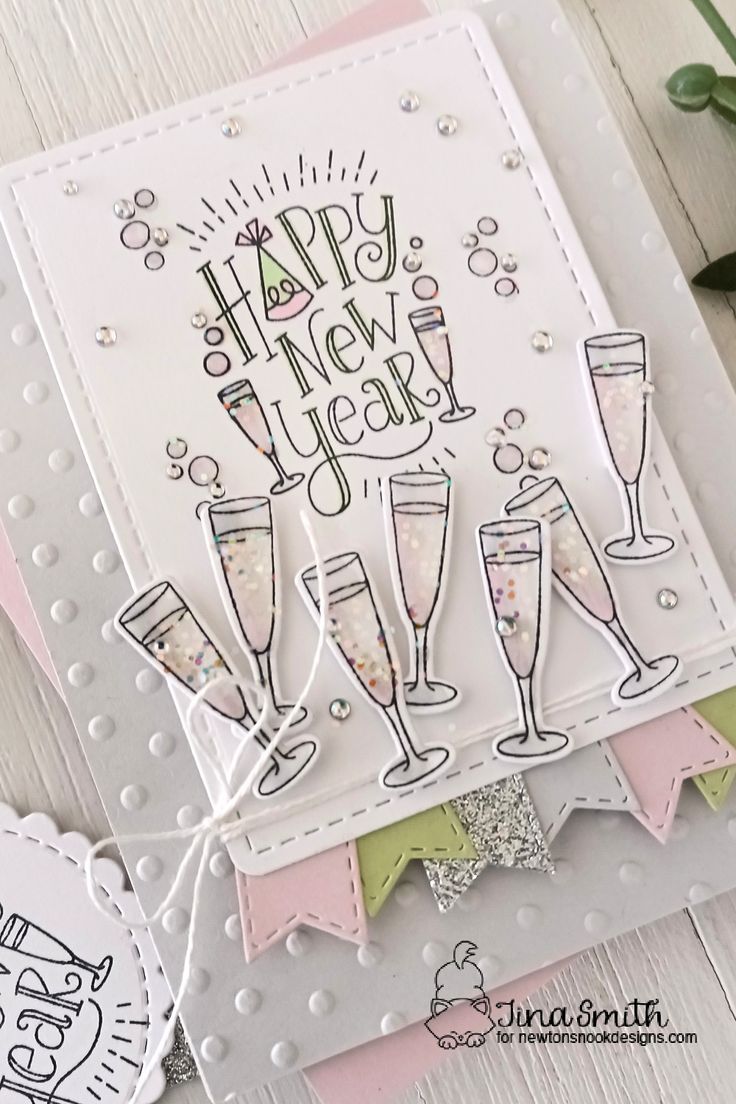 a happy new year card with wine glasses and bubbles on the bottom, next to an envelope