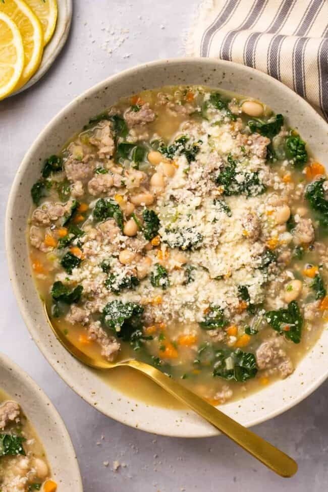 a bowl of soup with meat, vegetables and parmesan cheese on the side