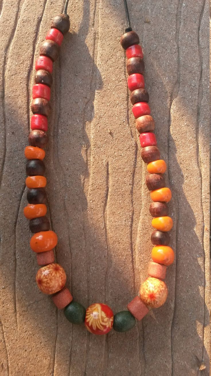 This slip-on, warm tone, wood bead necklace has a hippy feel to it.  It is made with mostly repurposed beads strung on a waxed black cord.  There are three accent beads, two of which have a red and cream floral pattern, the third of which has a dramatic red, cream, and orange stylized flower pattern. Cheap Orange Necklaces With Wooden Beads, Orange Wooden Beads For Festival, Orange Wooden Beads For Festivals, Adjustable Rustic Wooden Beaded Necklaces, Rustic Adjustable Wooden Beaded Necklaces, Large Brown Beads For Festival, Amber Bohemian Beaded Necklace With Wooden Beads, Bohemian Amber Beaded Necklace With Wooden Beads, Orange Wooden Beaded Necklaces For Beach