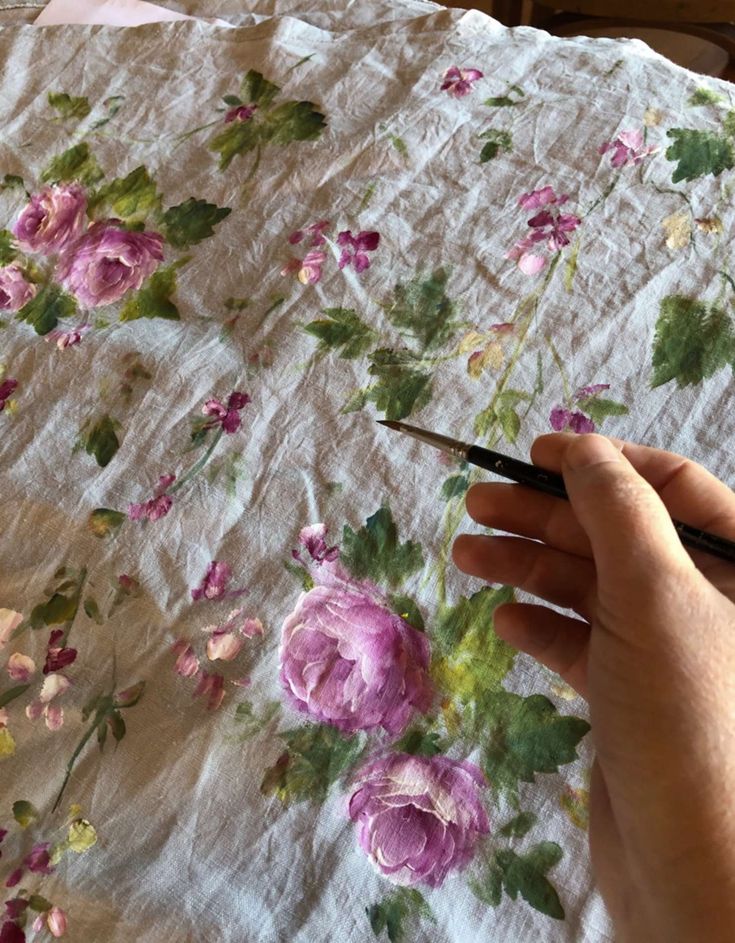 a hand holding a pair of scissors next to a flowered sheet with pink and green flowers on it