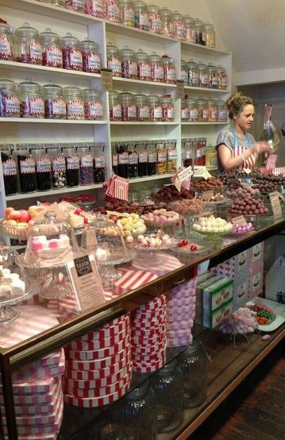 a woman standing in front of a counter filled with lots of cakes and cupcakes