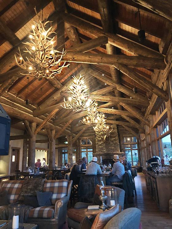 people are sitting at tables in a large room with wood beams and chandeliers hanging from the ceiling