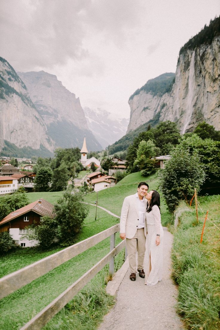 a bride and groom walking down a path in the mountains with houses on either side