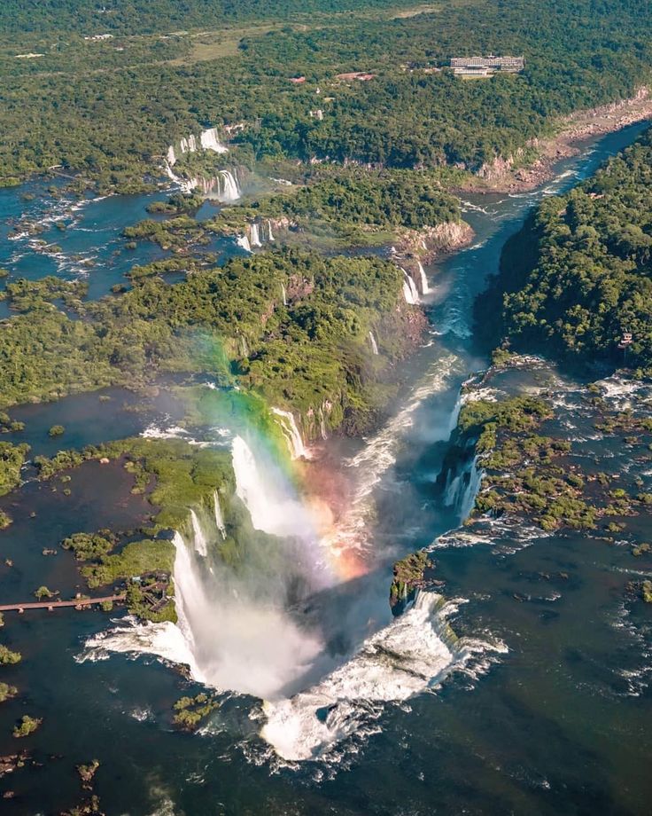 an aerial view of a waterfall with a rainbow in the middle and trees surrounding it