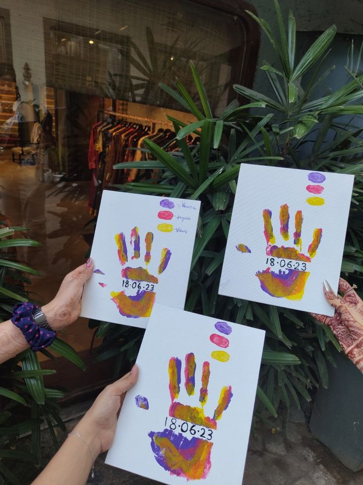 three people holding up hand prints in front of a store window with palm trees behind them